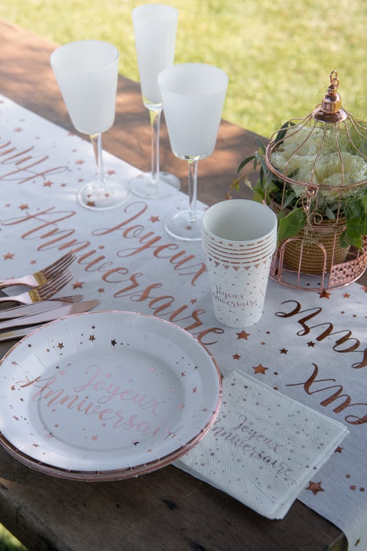 Mise en situation sur table du gobelet en carton Joyeux anniversaire rose gold à étoiles