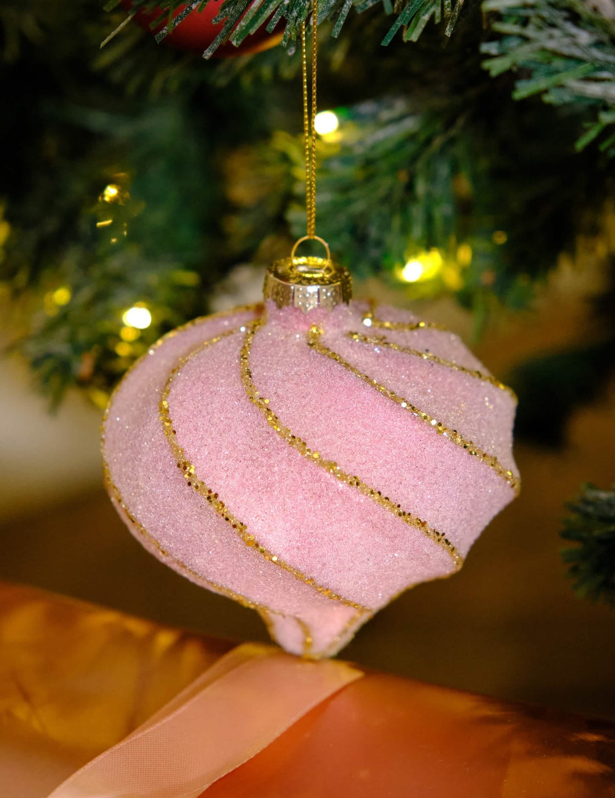 Primer plano de la bola de navidad en forma de gota con espirales rosa y dorado con purpurina
