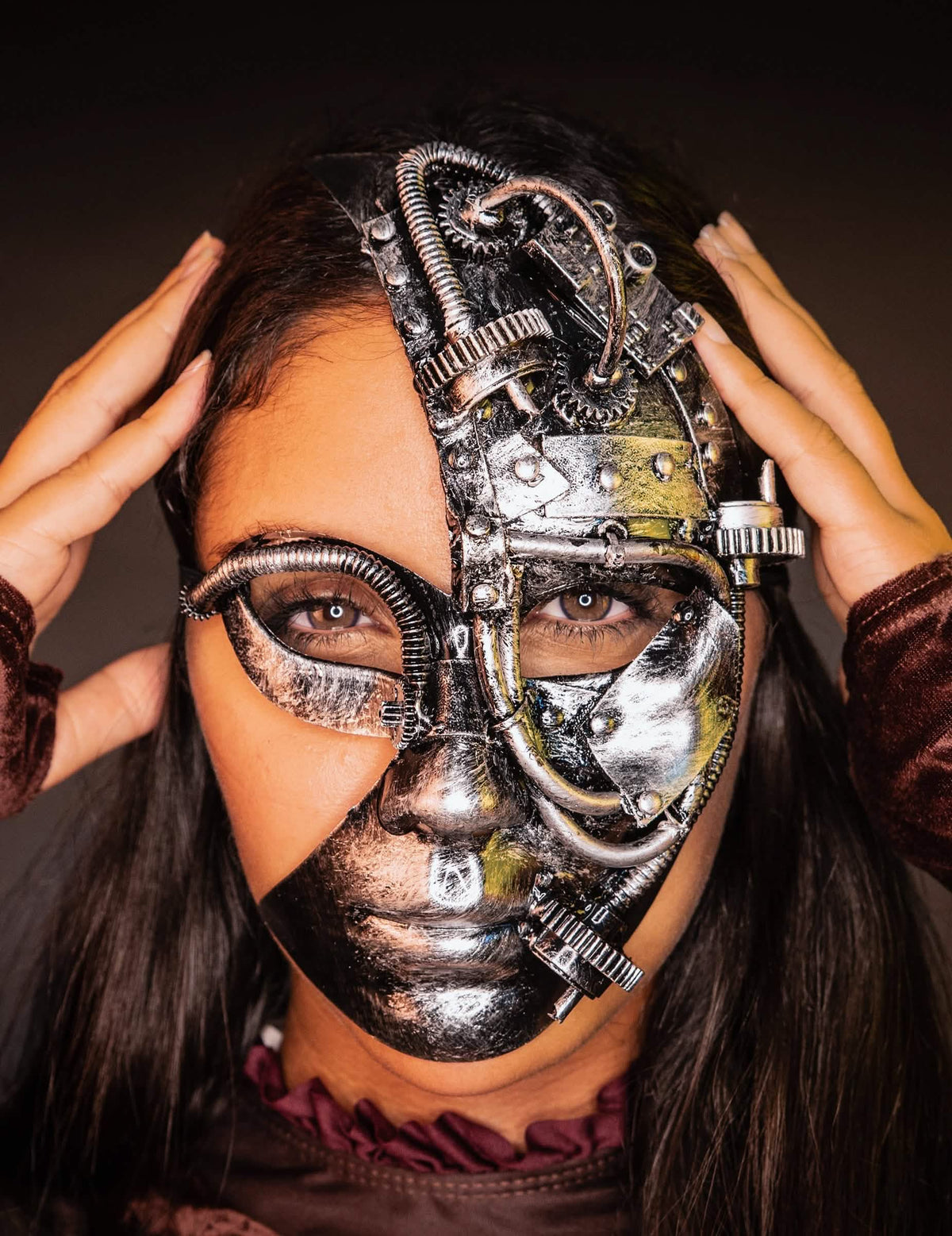 Vista de frente con las manos en las sienes de la media máscara robot steampunk