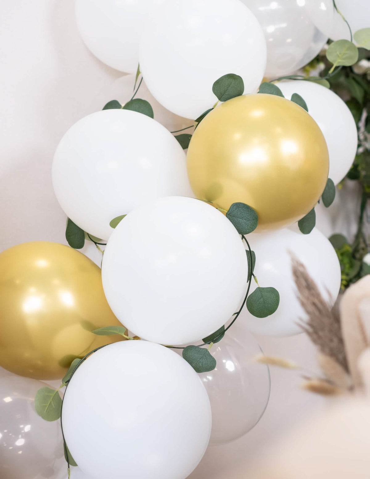 Primer plano de los globos y el follaje del kit de arco de 60 globos blanco y dorado con eucalipto vegetal