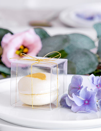 Gros plan sur le macaron et le ruban doré des petites boîtes pour cadeaux pour invités transparentes