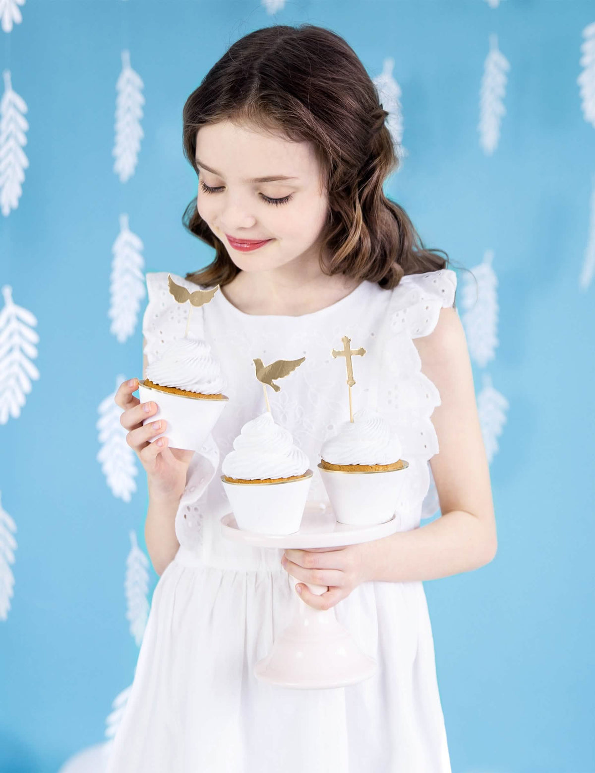 Escena de una niña sosteniendo los envoltorios para cupcakes de papel blancos y dorados para boda