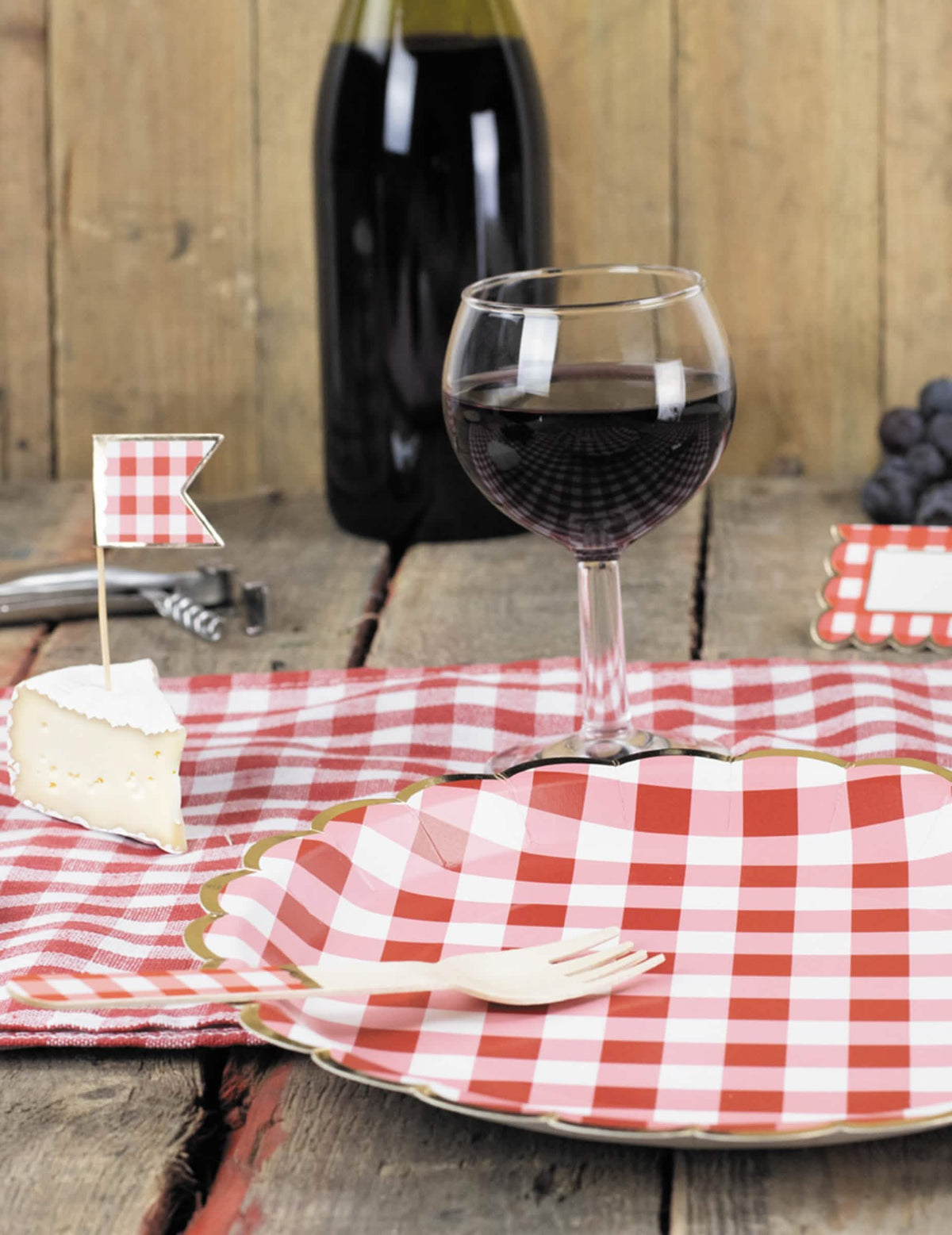 Mise en situation avec verre de vin et fourchette des assiettes festonnées en carton vichy rouge et blanc