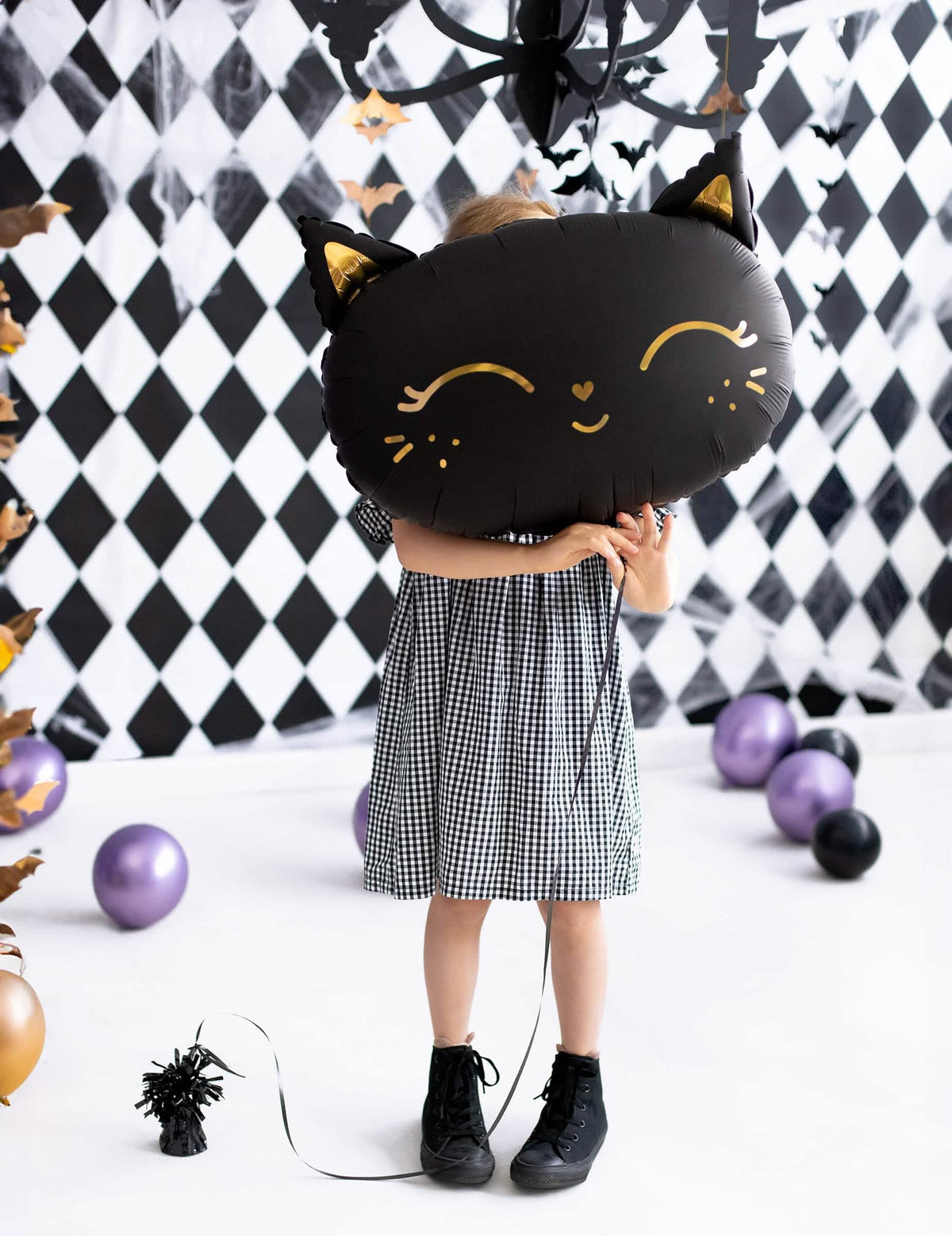 niño sosteniendo delante de su rostro el globo de aluminio gato para halloween