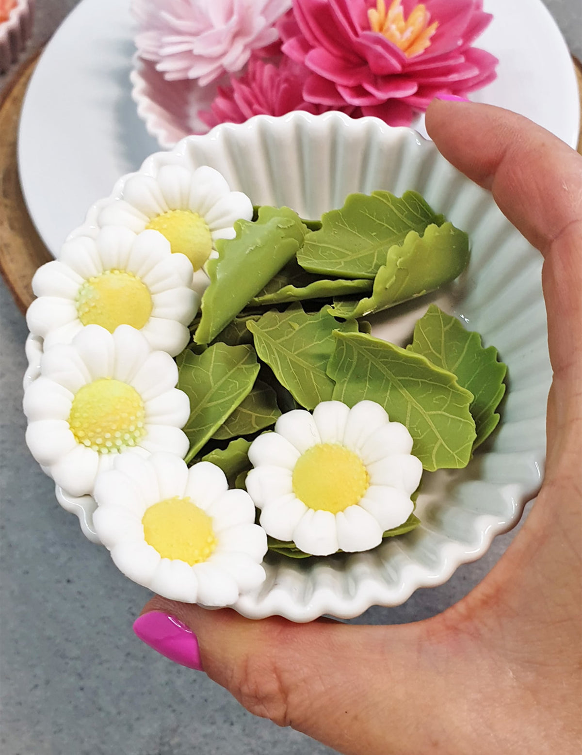 Mise en situation dans un ramequin des décorations en sucre marguerites et feuilles blanches et vertes