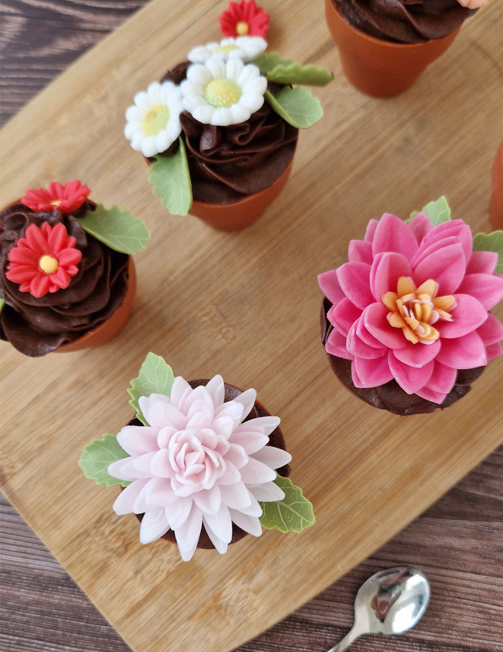 Mise en situation sur des cupcakes des décorations en sucre marguerites et feuilles blanches et vertes