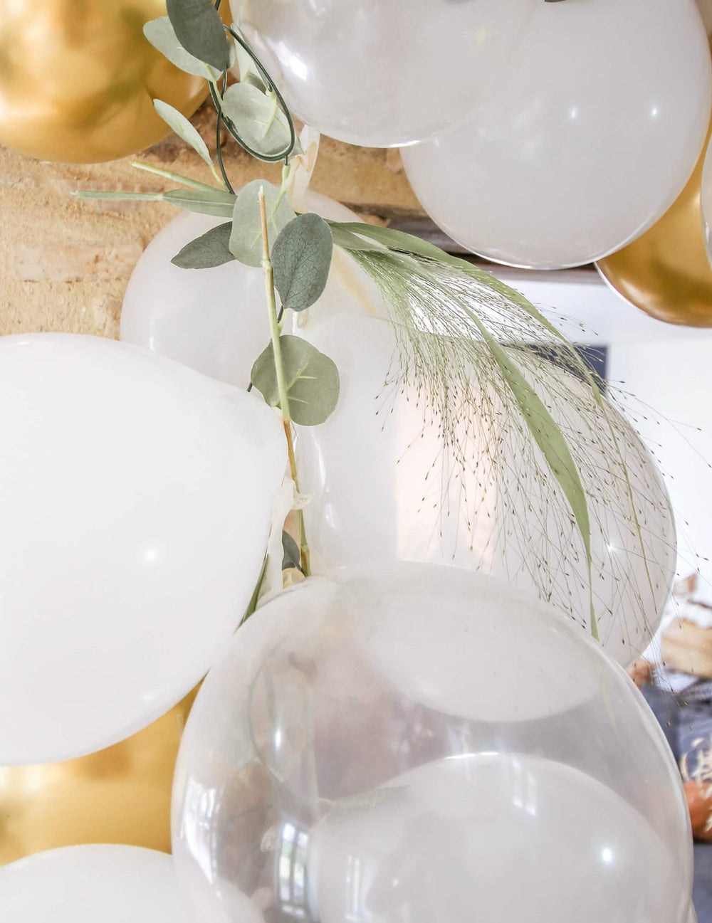Primer plano de la decoración vegetal del kit de arco de 60 globos blancos y dorado con eucalipto vegetal
