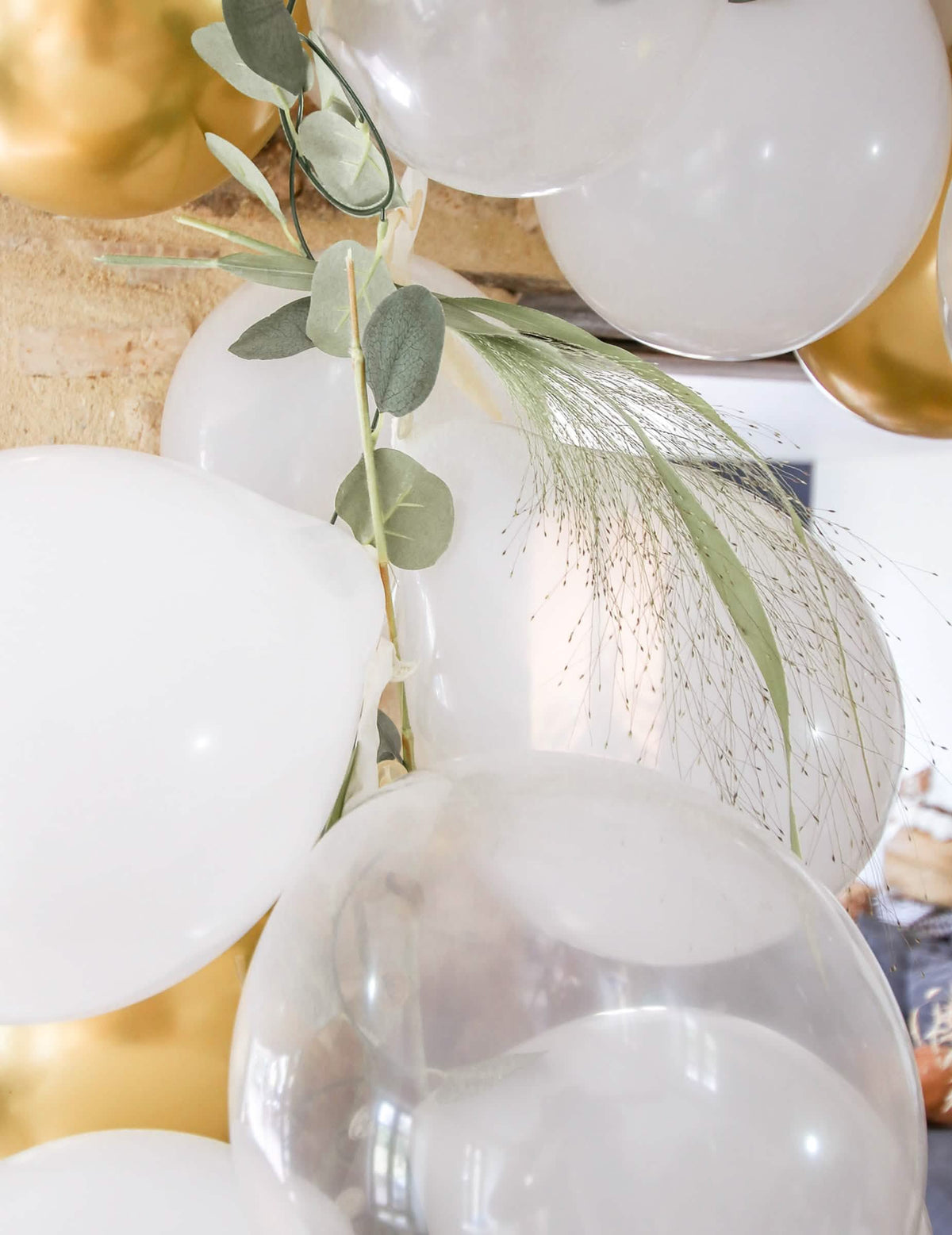 Primer plano de la decoración vegetal del kit de arco de 60 globos blancos y dorado con eucalipto vegetal
