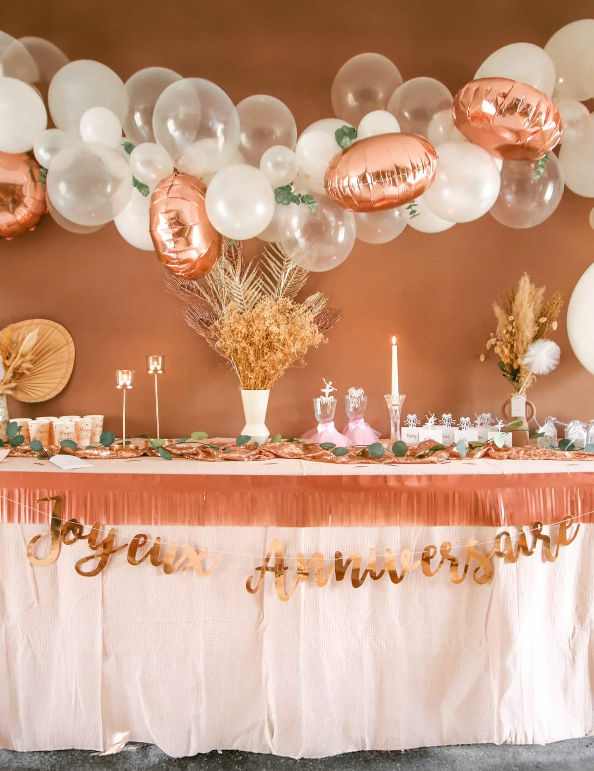 Mise en situación sobre una mesa de cumpleaños del kit arco de 70 globos oro rosa con eucalipto y rosas